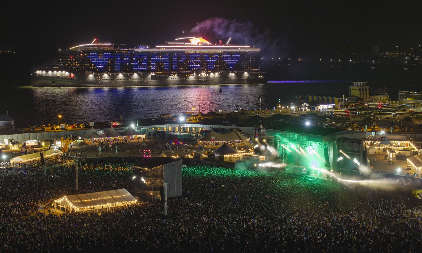 A cruise ship passing the Victorious Festival site, its lights illuminating the word 'Pompey' in blue