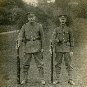 Conan Doyle standing with another man, both in military uniform with rifles at their side.